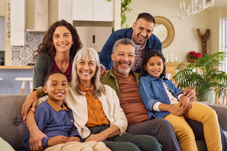 Portrait of happy family with grandmother and grandfather sitting on couch at home. Smiling parents, grandparents and happy multiethnic children looking at camera. Cheerful mixed race extended generational family having fun in the living room while smiling.
