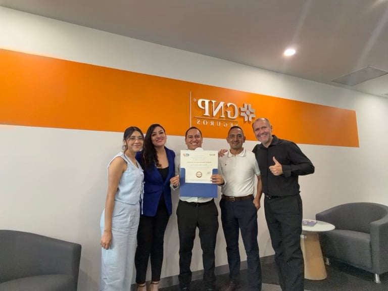 Five people standing together in front of an orange and white wall with logo, holding a certificate