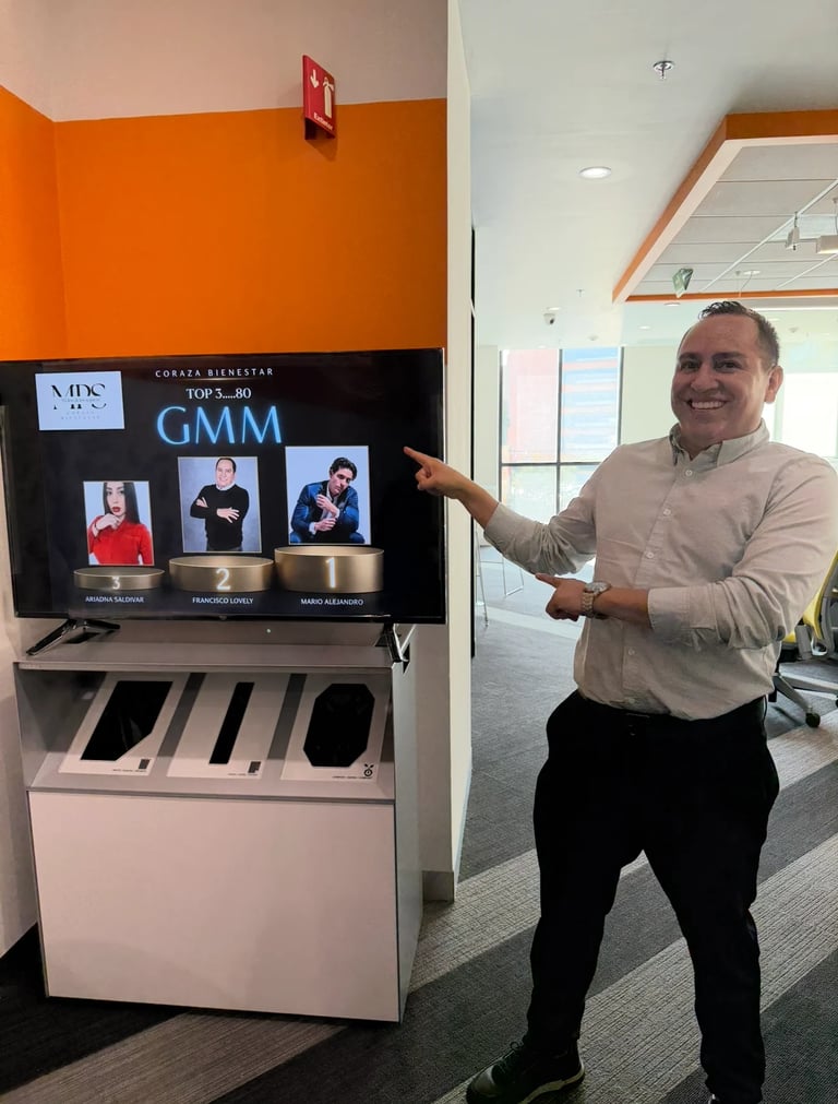 Man in beige shirt pointing to GMM display screen in modern office with orange accent wall