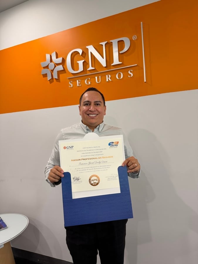 Man holding a professional certificate in front of a GNP Seguros branded orange wall